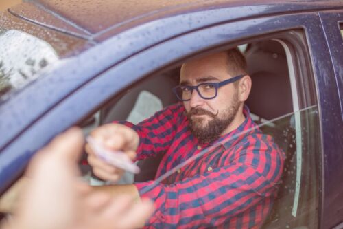Man sitting in car and giving his driving licence through the window. Visual concept for blog discussing how to get your license back after a dui/owi in Michigan.