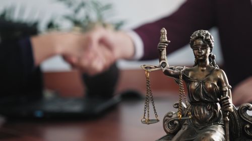 Statuette of lady justice on the table close-up against the background of the handshake of a woman and a man