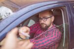 Man sitting in car and giving his driving licence through the window. Visual concept for blog discussing how to get your license back after a dui/owi in Michigan.